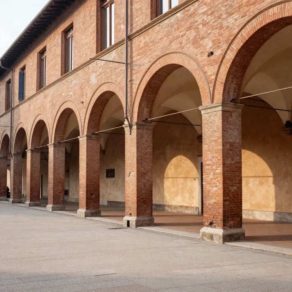 Portici di Bologna in mattoni al tramonto, con piazza chiara e foschia calda.